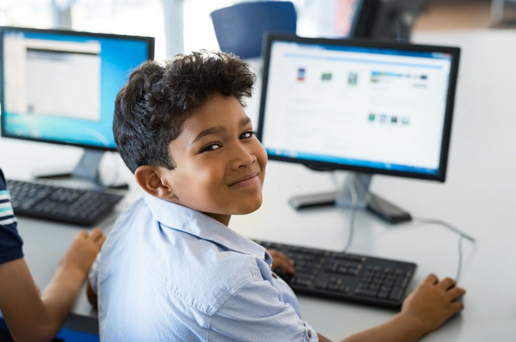 Young happy schoolboy using computer to search interne